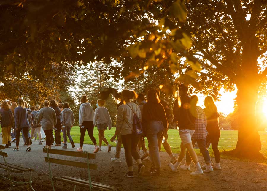 Students walking on a path in a cemetery with the sun setting behind them