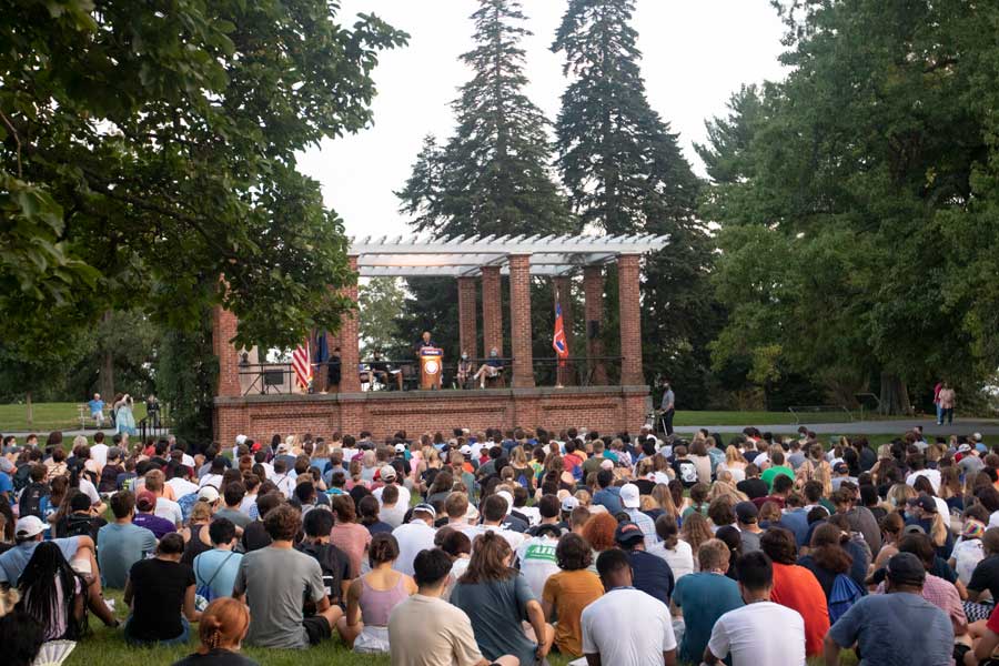 The Class of 2025 sitting in front of an outdoor stage with a speaker at the podium