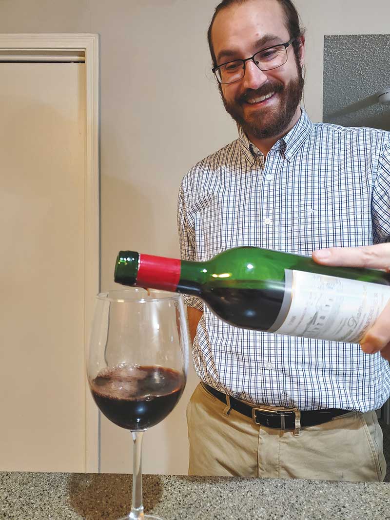 Man watching another person pouring a glass of red wine