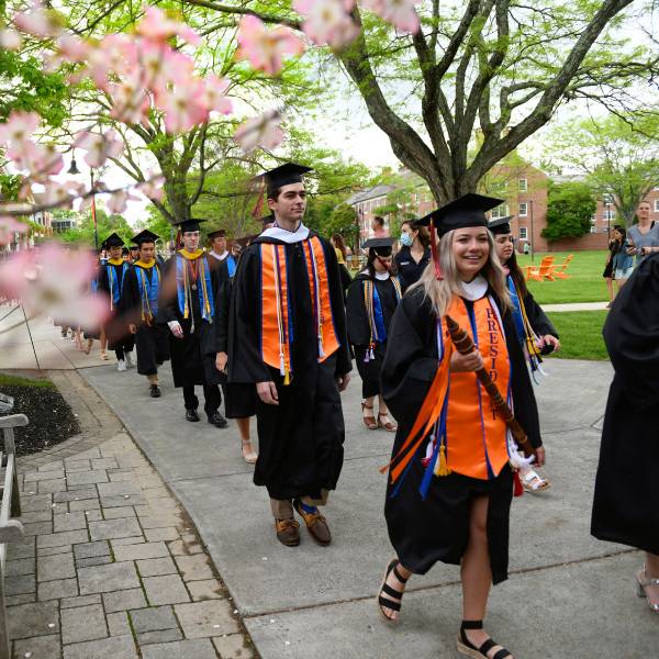 Gettysburg College graduates walking on an outdoor path towards Penn Hall