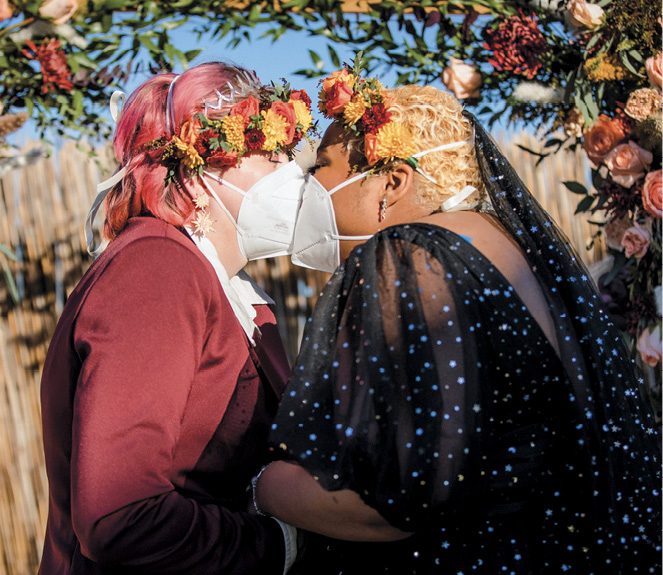 Two women kissing with masks on at a wedding