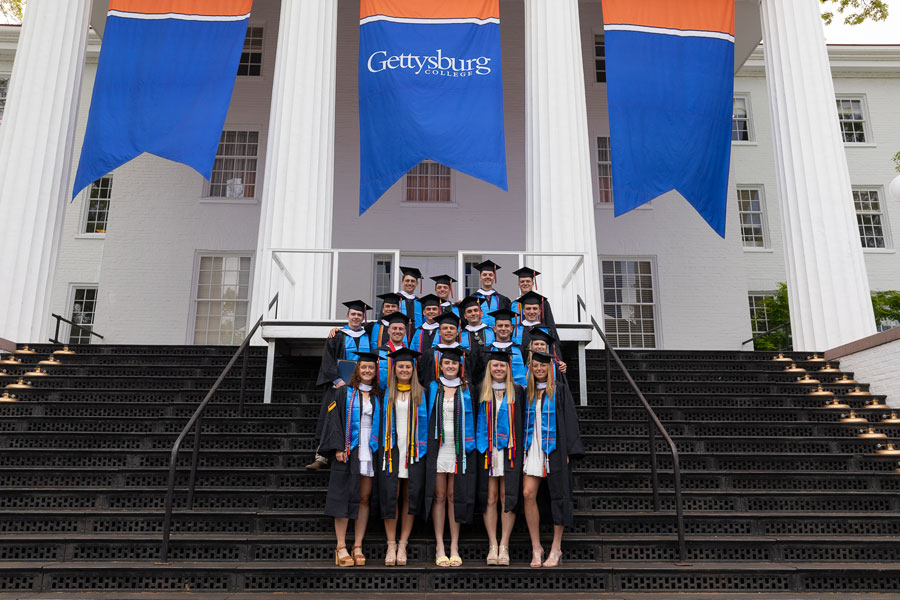 Graduates standing on the steps of Penn Hall underneath banners