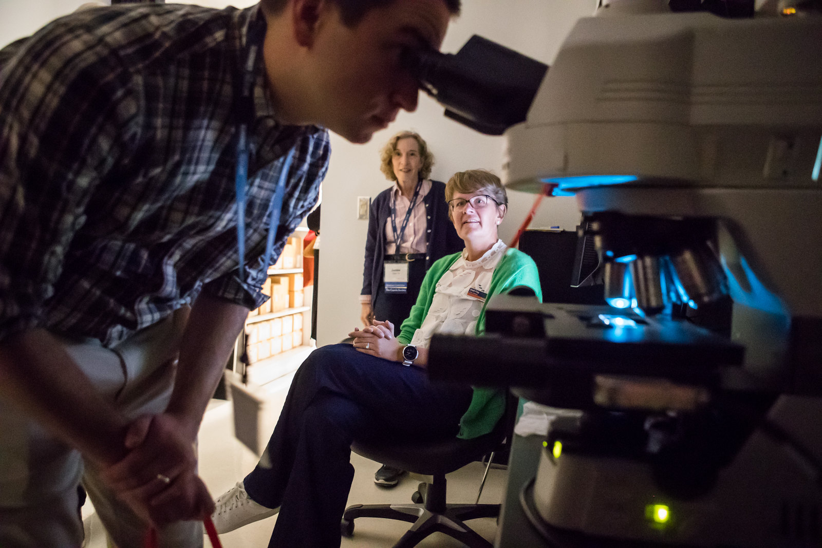 Male student peers into microscope with faculty looking on