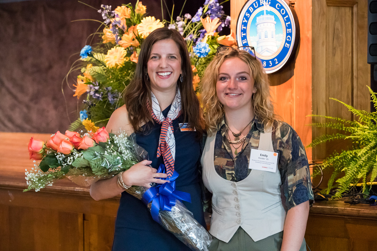 Two young ladies smile while one holds a bouquet of roses