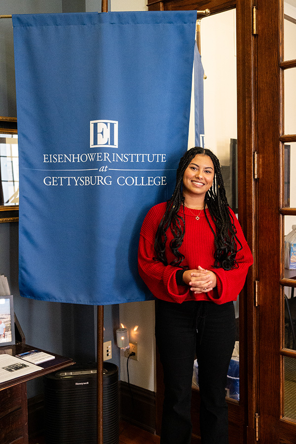 Meriem stands in front of the Eisenhower Institute flag