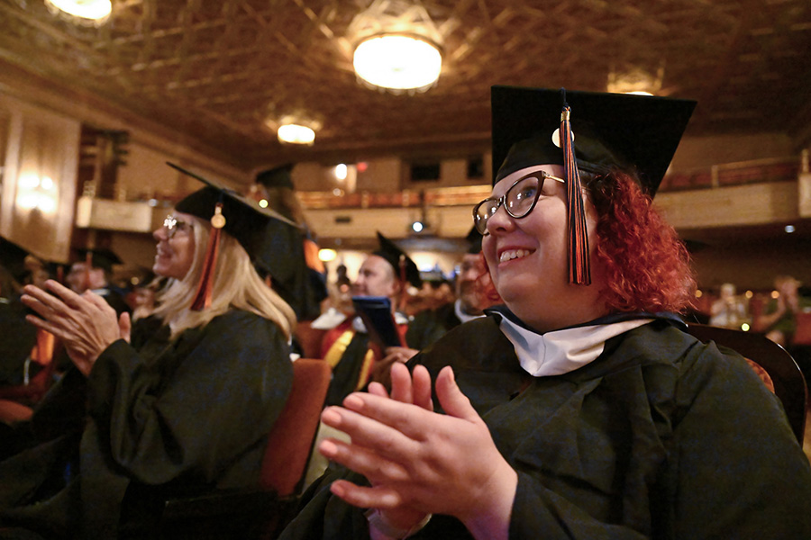 A photo of Graduates applauding as their classmates walk across the stage 