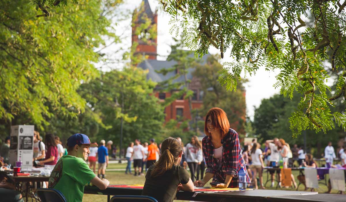 Student signing up for an activity at an activity fair with Glatfelter Hall in the background