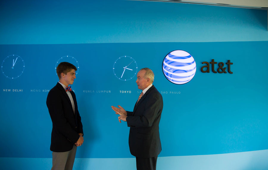 Student standing in front of a wall of clocks with a man in a suit speaking to him