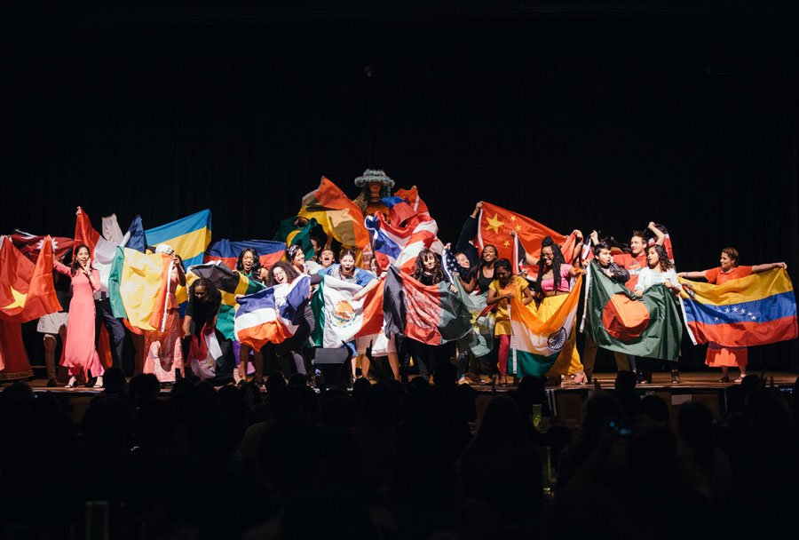 Students on a stage holding flags from different countries around the world
