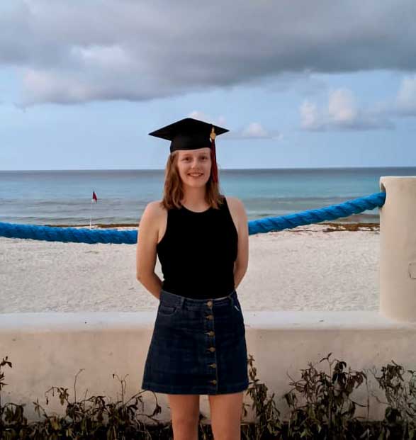 Cailin Casey standing in front of a beach wearing a graduation cap