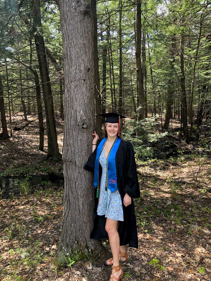 Cailin Casey standing in a forest with her cap and gown