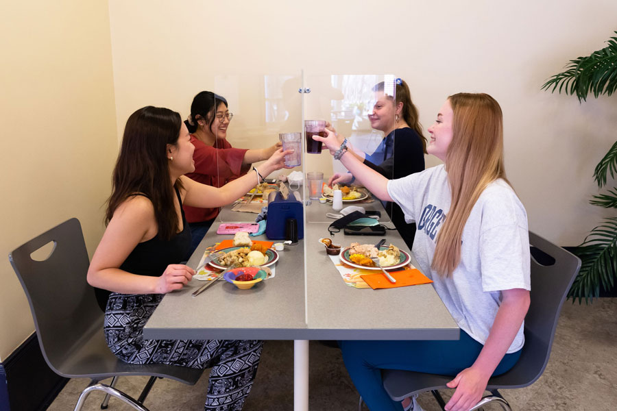 A group of friends doing a cheers with a plexiglass barrier between them