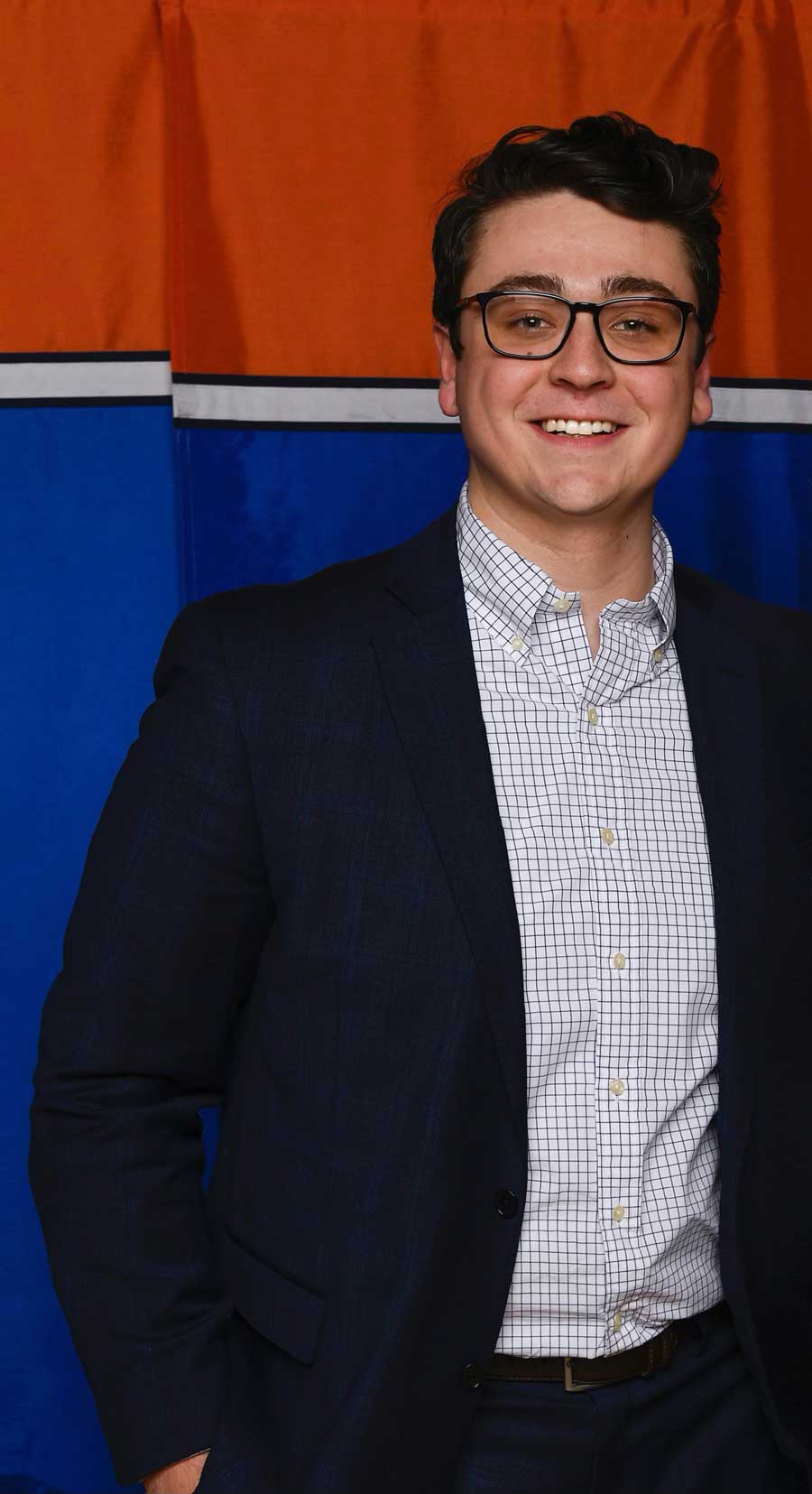 Colin Hetherington in a suit in front of a blue and orange banner