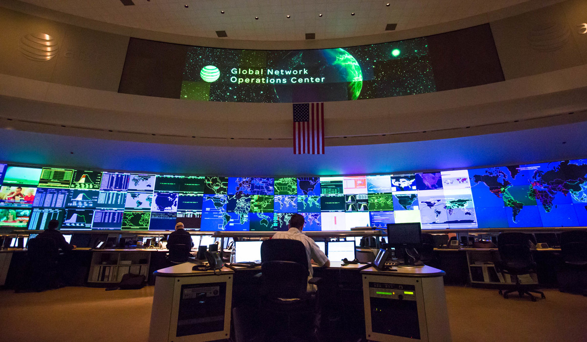 People sitting at their desks with a large and wide computer screen at the front of the room inside the AT&T global network operations center