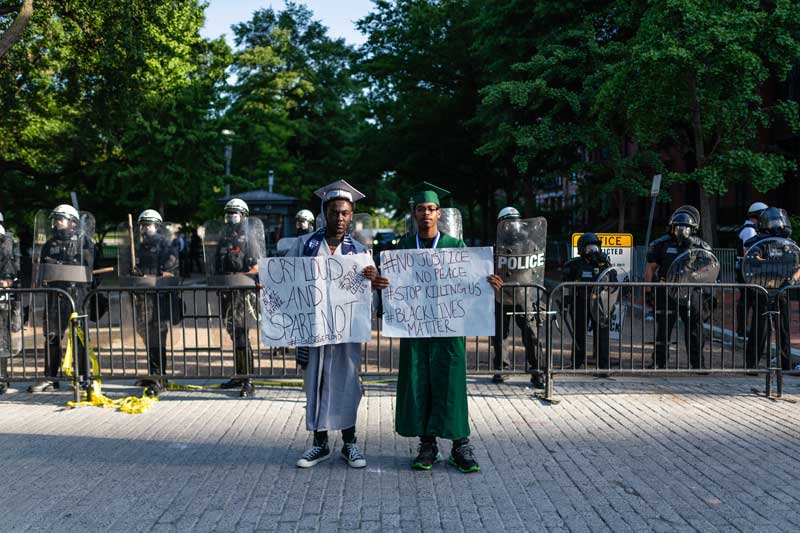 Two college graduates standing with signs in front of police