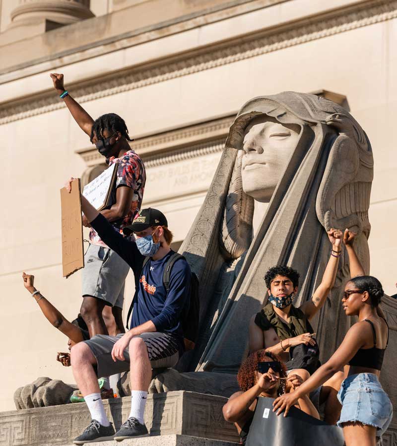 Demonstrators sitting next to a DC monument with raised fists and signs