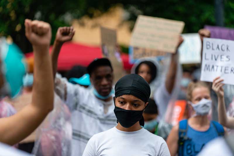 Demonstrator looking towards the ground with people around them raising their arms with signs