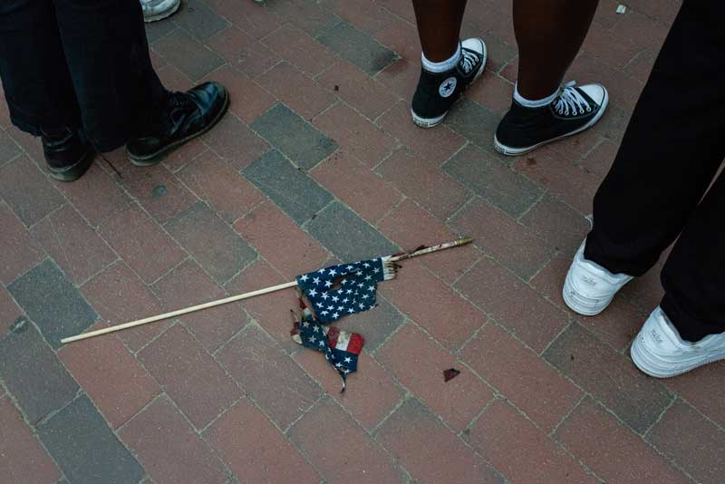 Protestors standing with a tattered American flag on the ground