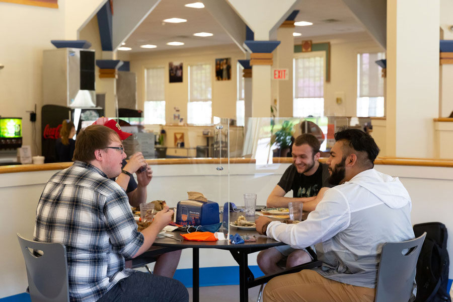 Group of four students eating together with a plexiglass barrier