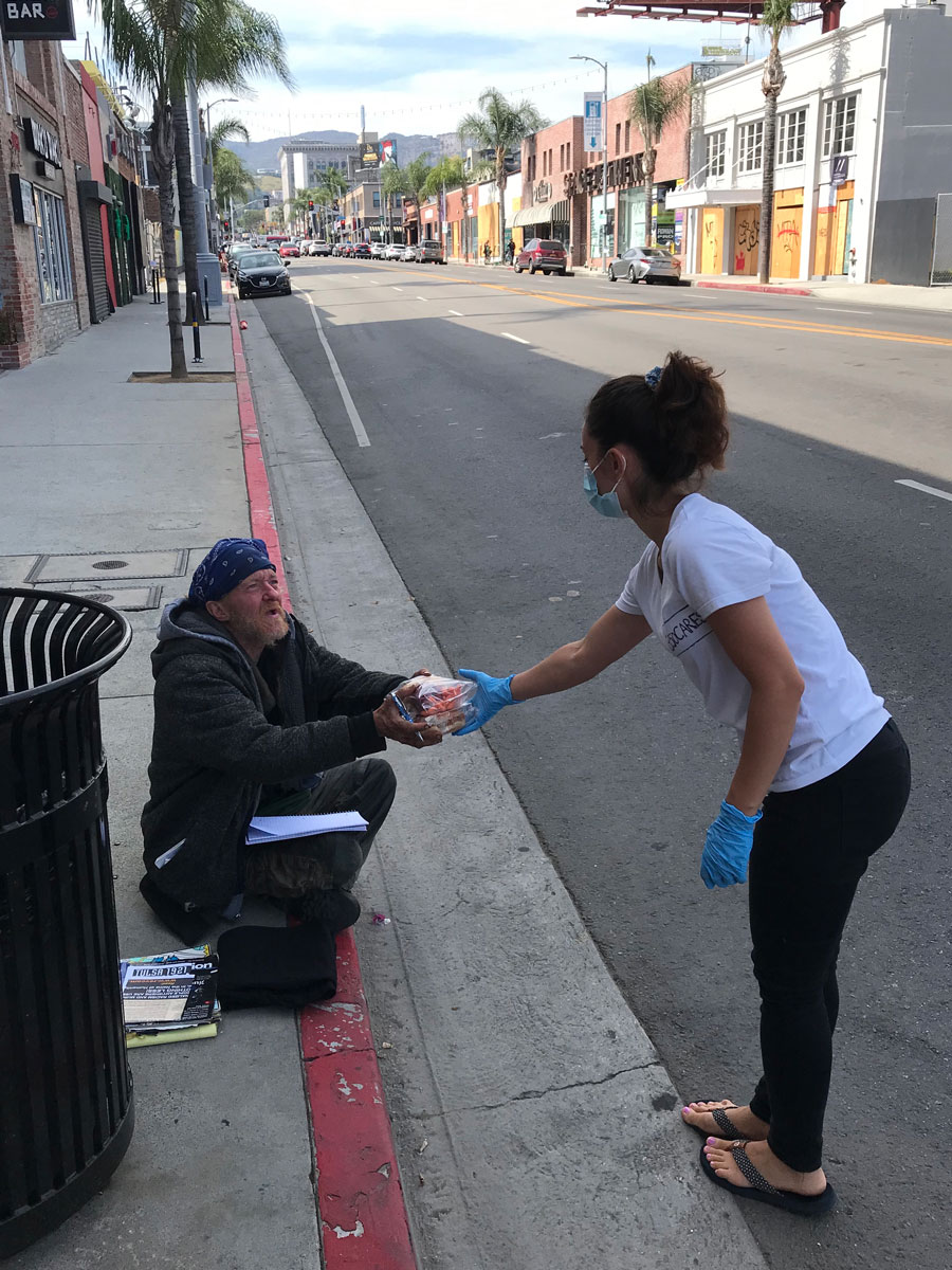 Hamasa Ebadi handing a homeless man a package of food in downtown Los Angeles