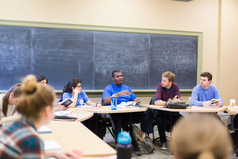 Students sitting at desks in a classroom with a chalkboard at the back of the room