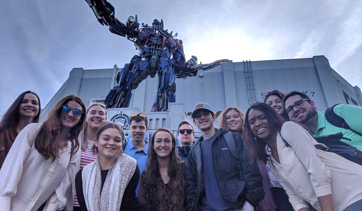 group crouches for a photo under an Optimus Prime statue