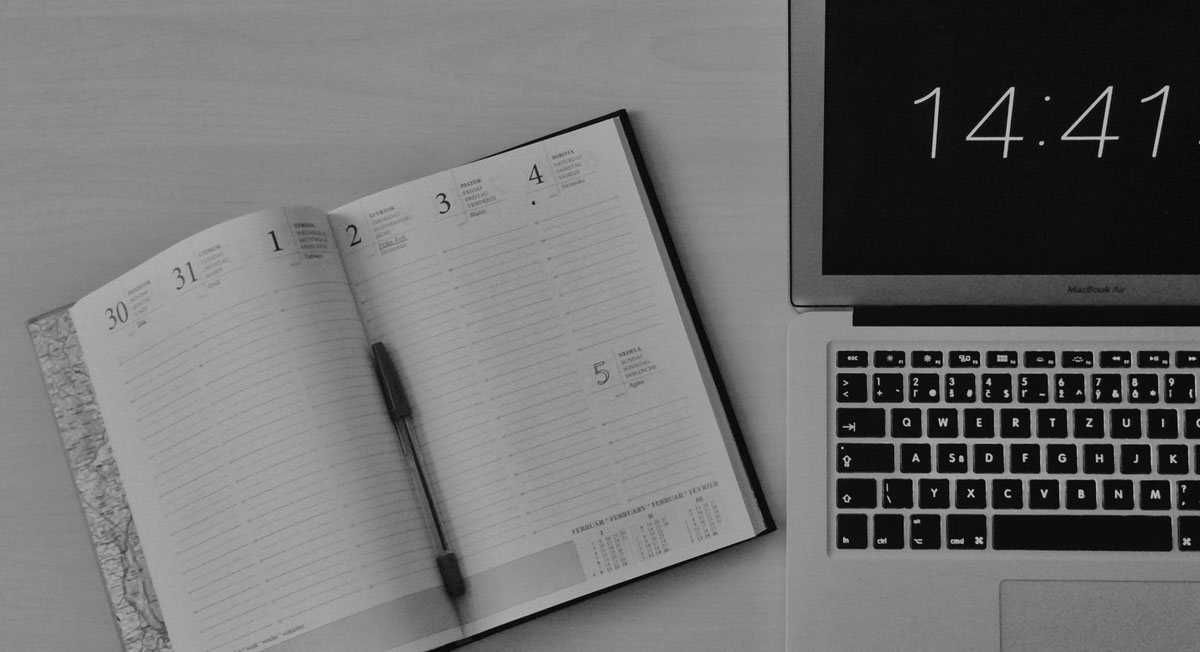 Photo of a day by day planner with a laptop beside it displaying the time