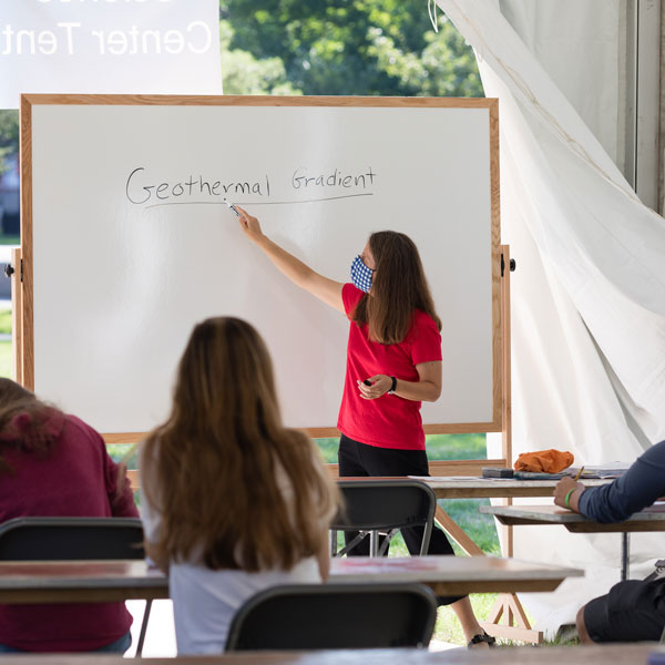 Teacher writing on a dry erase board in a tent style classroom