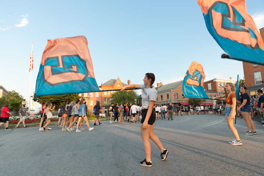 Students walking through Lincoln Square with other students waving Gettysburg College flags