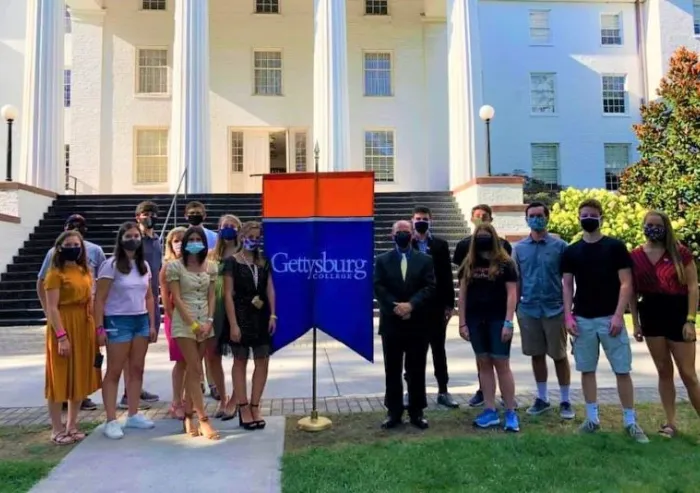 High school age students standing outside Penn Hall with a Gettysburg Banner