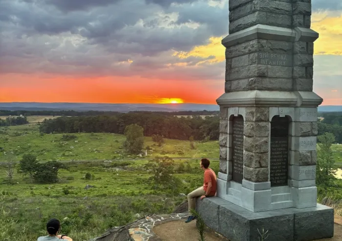 Visitors sit beside a Gettysburg battlefield monument at sunset.