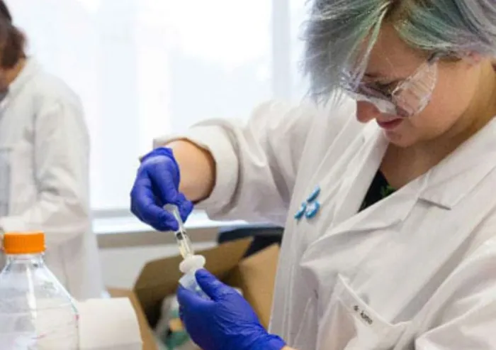 Student in protective clothing and gloves handling a laboratory sample.