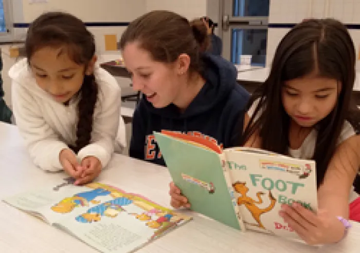 A student reads books with a pair of small children.