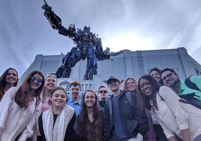 A group of people poses for a selfie in front of a large robot statue outside a building