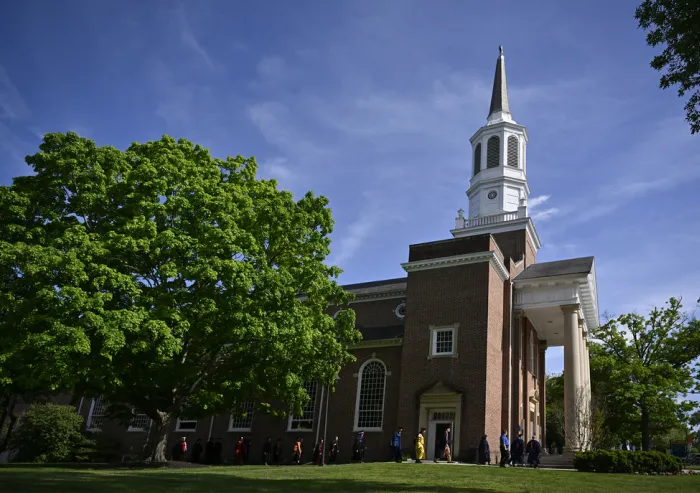 Graduates gather outside a historic brick church with a tall white steeple.