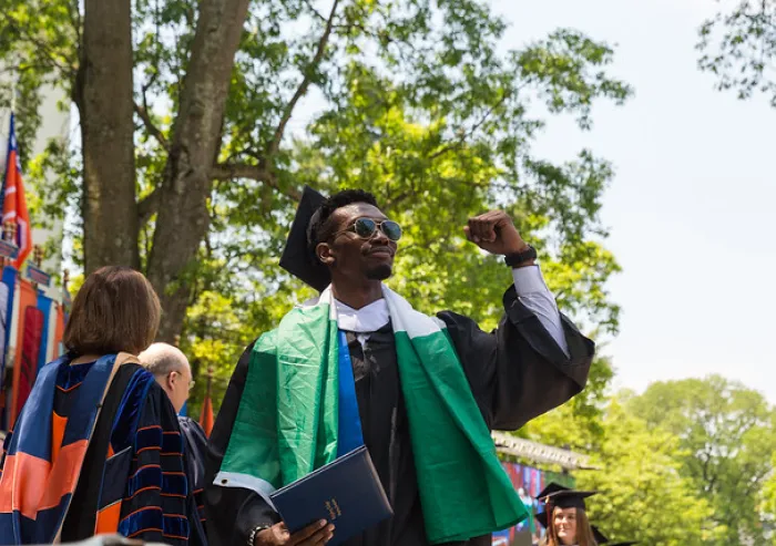Graduate celebrates outdoors with a raised fist and diploma.