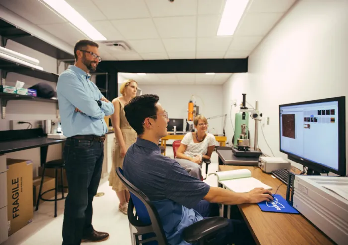 Students and Professors work with laboratory equipment and computer monitors.