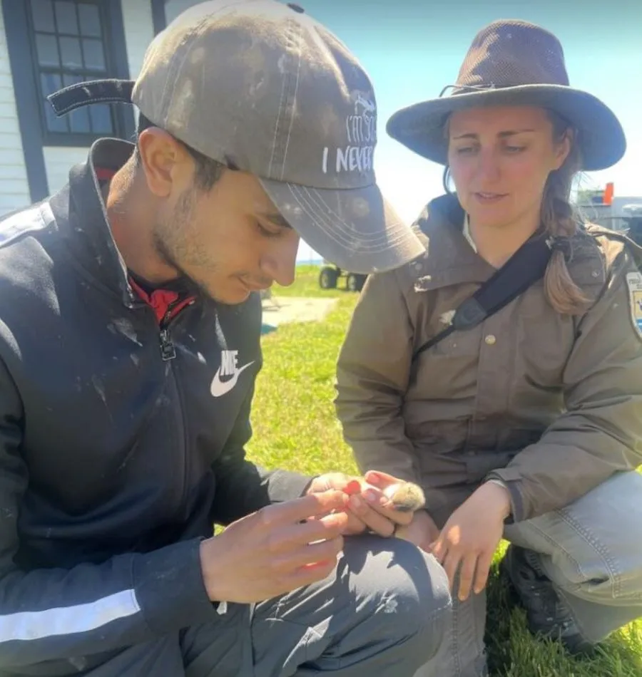 male student handles young bird as woman looks on