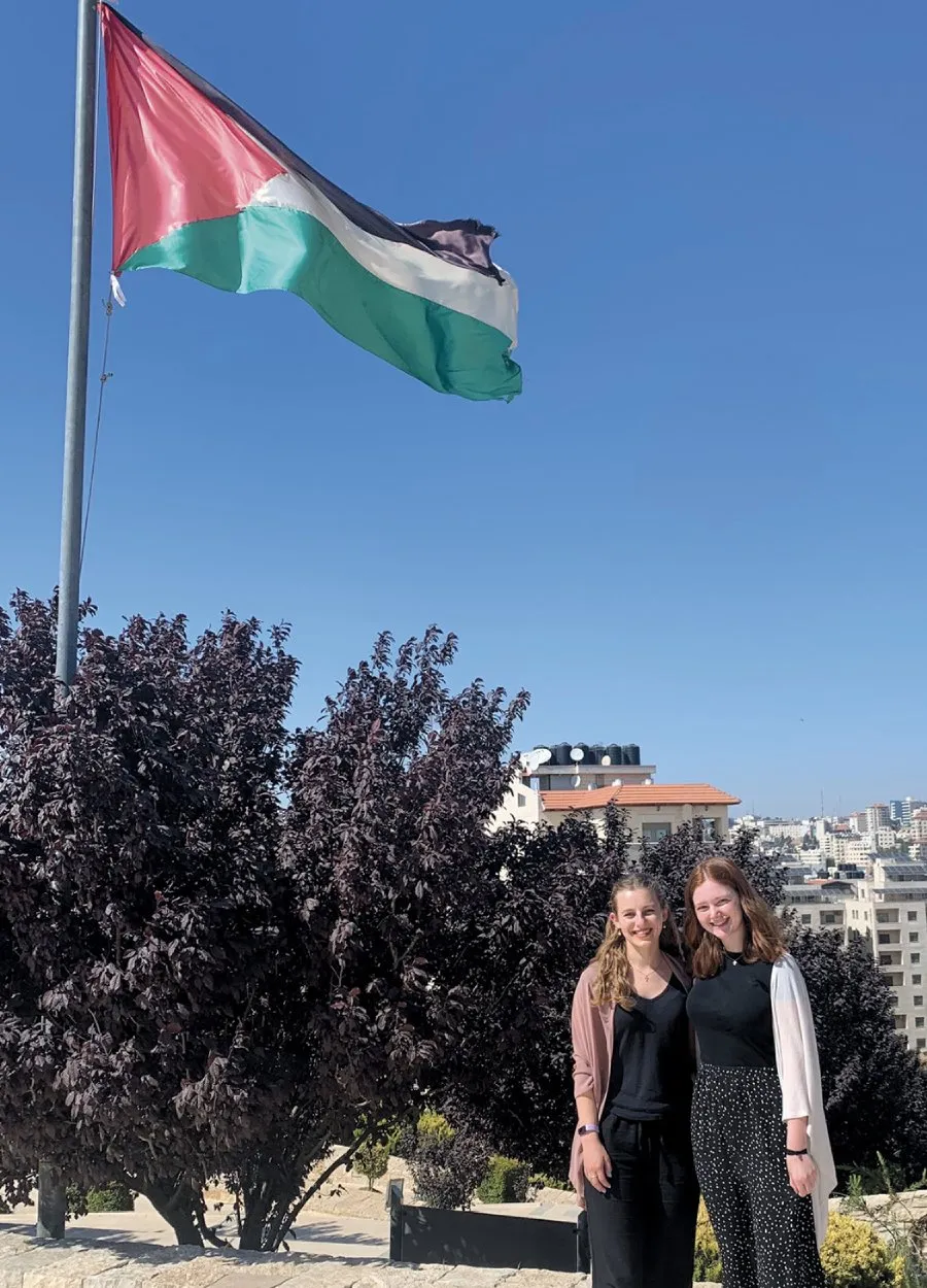 two female students standing in international location beneath flag