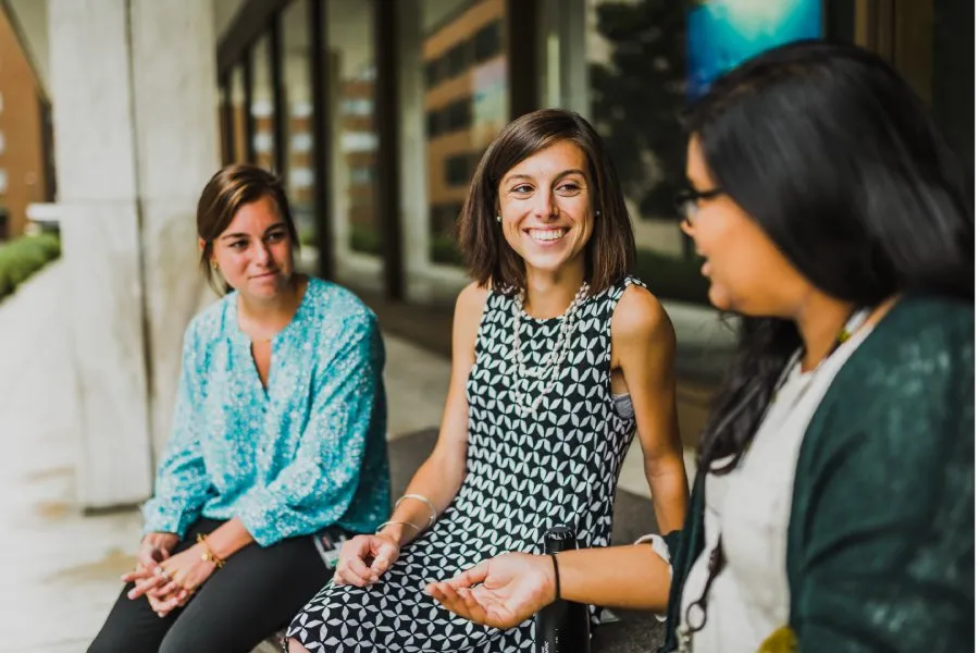 women smile and talk together seated outside