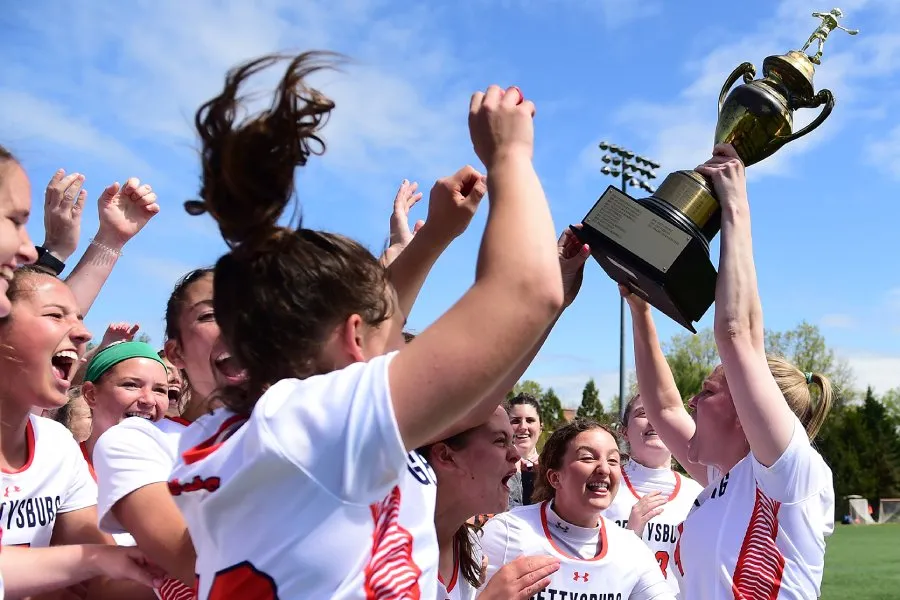 womens lacrosse team celebrates and holds trophy up