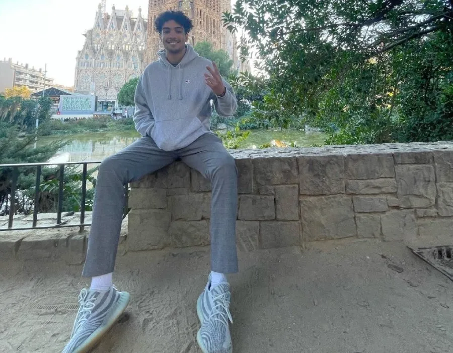 male student poses seated on stone wall in front of ornate cathedral