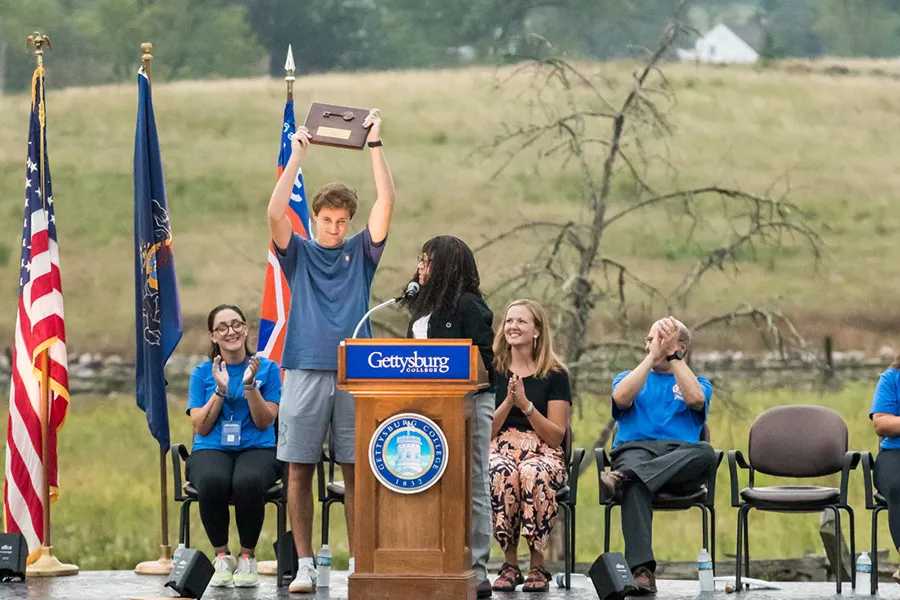 student holds up key to town on stage behind podium