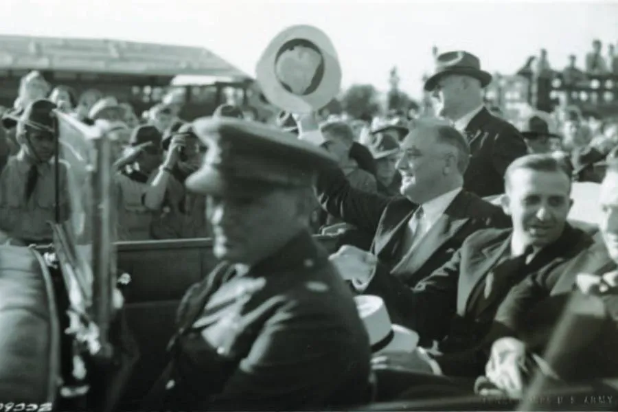 black and white photo of President Eisenhower lifting hat in back seat of car in parade