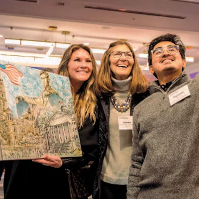 woman holds painting alongside friend taking selfie