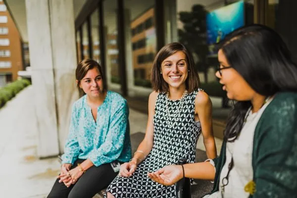 women smile and talk together seated outside