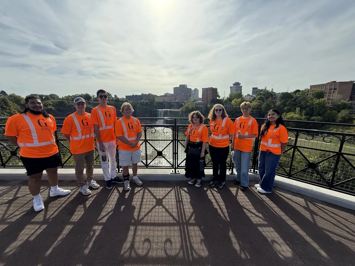 students in bright shirts smile in front of waterfall at edge of city