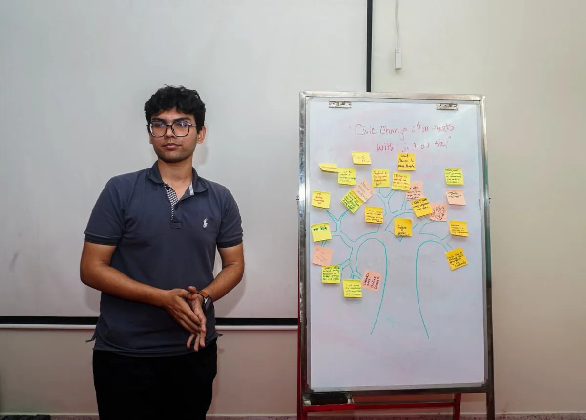 male student stands in front of dry erase board with sketched tree and post-it notes