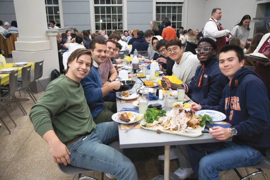 group of students sitting at dining hall table together smile for camera