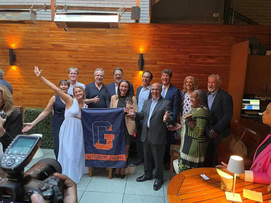 Caroline Glennon ’19 holding a flag with alumni and campus leaders at a retirement celebration.